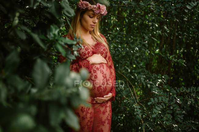 Femme enceinte avec les yeux fermés touchant le ventre tout en se tenant dans le jardin dans une journée ensoleillée — Photo de stock