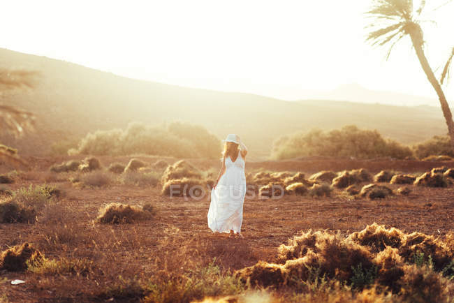 Mulher de vestido branco em campo seco à luz do sol — Fotografia de Stock
