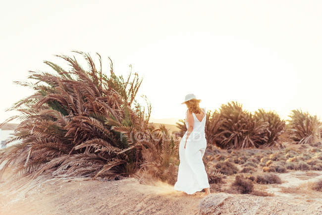 Mujer vestida de blanco caminando en campo seco a la luz del sol en España - foto de stock