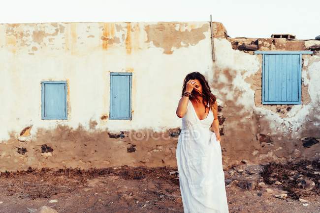 Femme en robe blanche marchant à l'extérieur par une vieille maison — Photo de stock