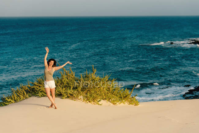 Donna attiva in pantaloncini bianchi in posa con le braccia distese sulla spiaggia di sabbia — Foto stock