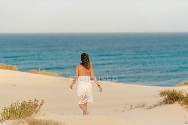 Mulher ativa em vestido branco andando praia arenosa — Fotografia de Stock
