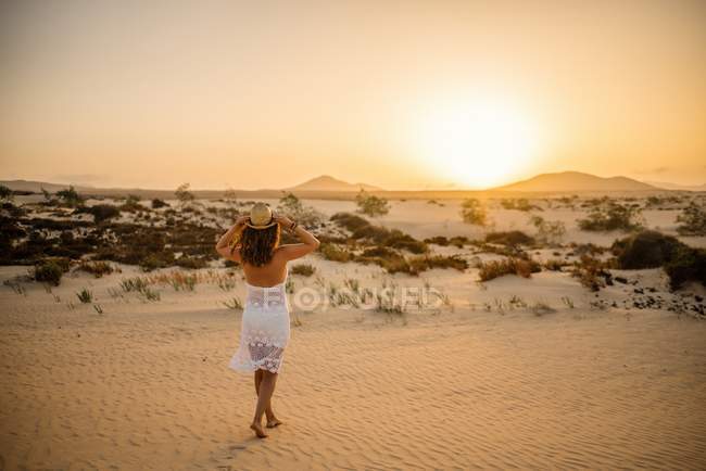 Mujer activa en vestido blanco caminando en desierto seco descalzo - foto de stock