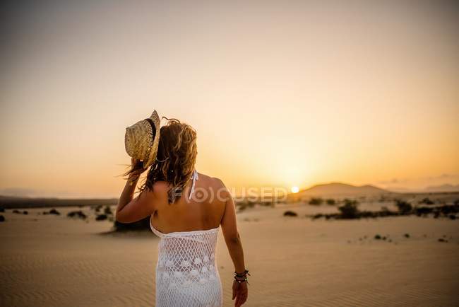 Woman throwing hat into distance to sun in sandy landscape — Stock Photo