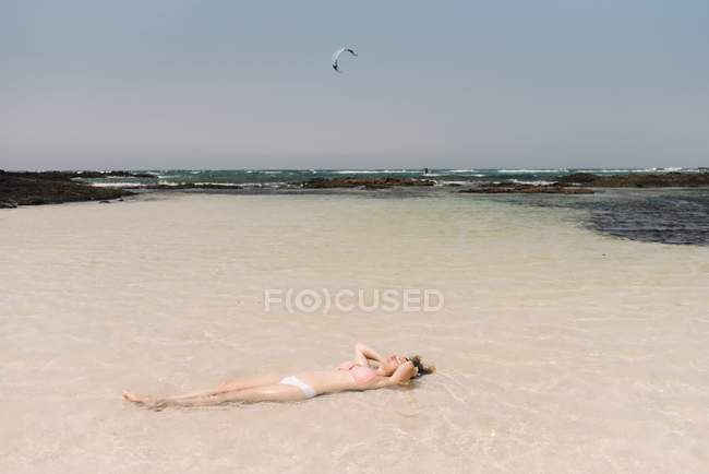 Женщина в купальнике лежит в воде на берегу моря — стоковое фото