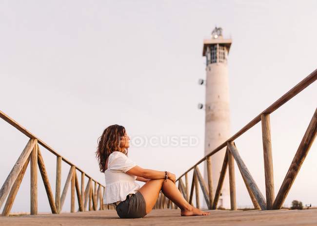 Donna seduta sul ponte verso il faro e che distoglie lo sguardo — Foto stock