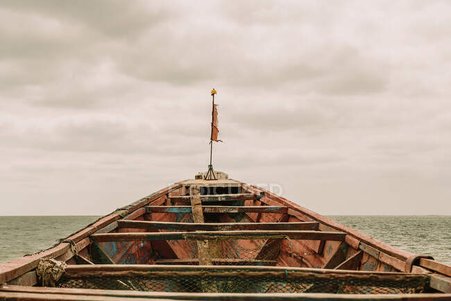 Altes schäbiges Schiff mit Flagge schwimmt auf plätscherndem Meerwasser gegen bewölkten Himmel in Gambia — Stockfoto