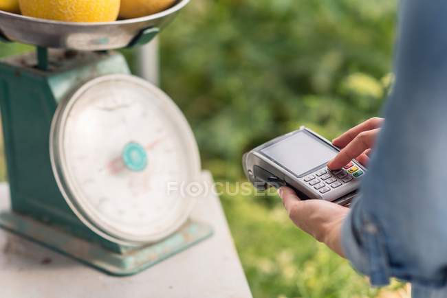Imagen recortada de la mujer que pesa melones y facturación durante el uso de terminal para el contacto menos pago - foto de stock