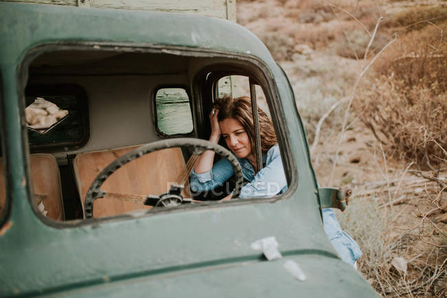 Thoughtful young woman in denim shirt leaning in window of green truck — Stock Photo