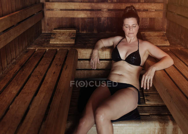 slaap Encyclopedie Ideaal Woman in black bikini sitting with closed eyes on towel in steam room  leaning on wooden bench and enjoying heat — resting, spa - Stock Photo |  #313128644