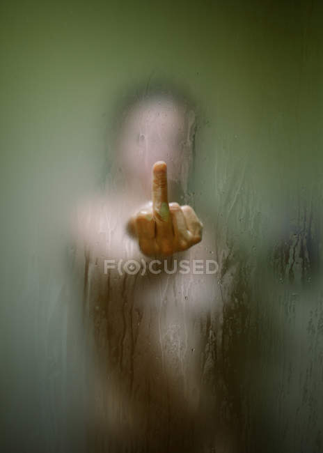 Through wet glass view of unrecognizable woman showing middle finger while taking shower — Stock Photo