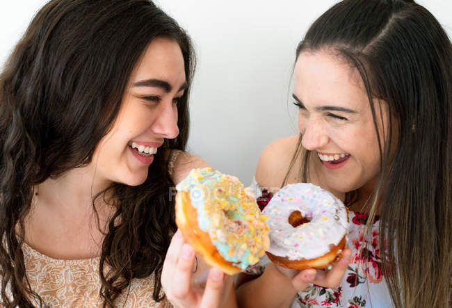 Щасливі жінки їдять глазуровані десерти на білій стіні — стокове фото