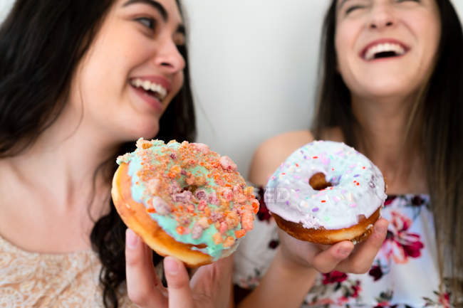 Happy women eating glazed desserts in a white wall — Stock Photo
