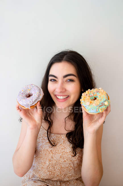 Femme insouciante s'amuser et jouer avec des pâtisseries glacées avec des aspersions tout en se tenant par mur blanc — Photo de stock