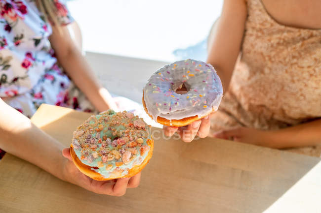 Cropped from above women carrying round glazed pastries with sprinkles while sitting by table — Stock Photo