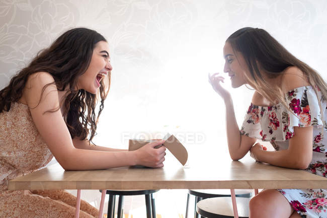 Счастливые женщины в сарафанах с коробкой застекленных десертов, сидящих за столом — стоковое фото