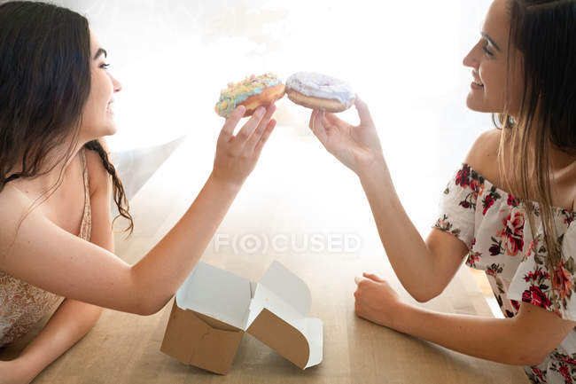 Happy women in sundresses with box of glazed desserts sitting at table — Stock Photo