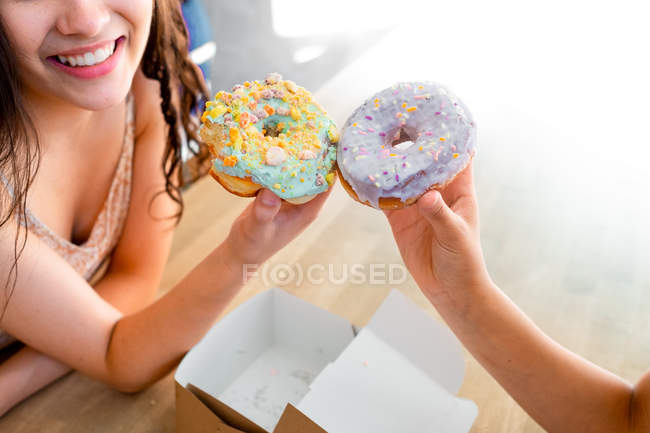 Cropped female hands carrying round glazed pastries with sprinkles while sitting by table — Stock Photo