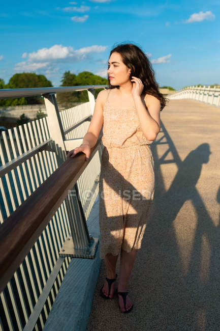 Розслаблена жінка в вечірній час прогулюється по мосту в сонячний вітряний день — стокове фото