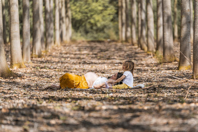 Madre embarazada e hija pequeña descansando en el suelo en el parque - foto de stock