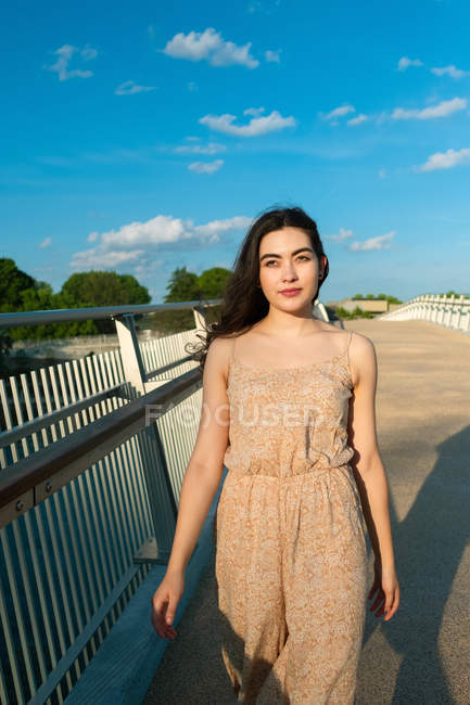 Relaxed woman in sundress strolling along bridge on sunny windy daytime — Stock Photo
