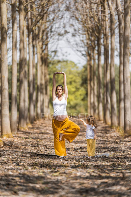 Allegro incinta madre e figlia praticare yoga nel parco durante il sole diurno — Foto stock