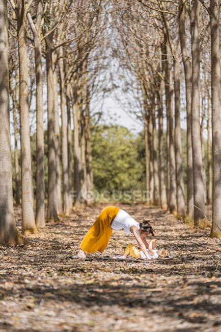 Mãe grávida alegre praticando ioga posar com a filha no parque durante o dia ensolarado — Fotografia de Stock