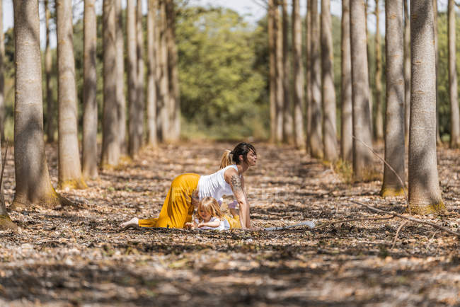 Alegre madre embarazada e hija practicando yoga en el parque durante el clima soleado - foto de stock