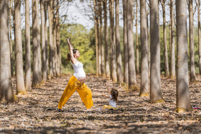 Fröhliche schwangere Mutter und Tochter praktizieren bei sonnigem Wetter Yoga im Park — Stockfoto