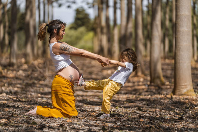 Schwangere Mutter und kleine Tochter haben Spaß und halten Händchen im Park — Stockfoto