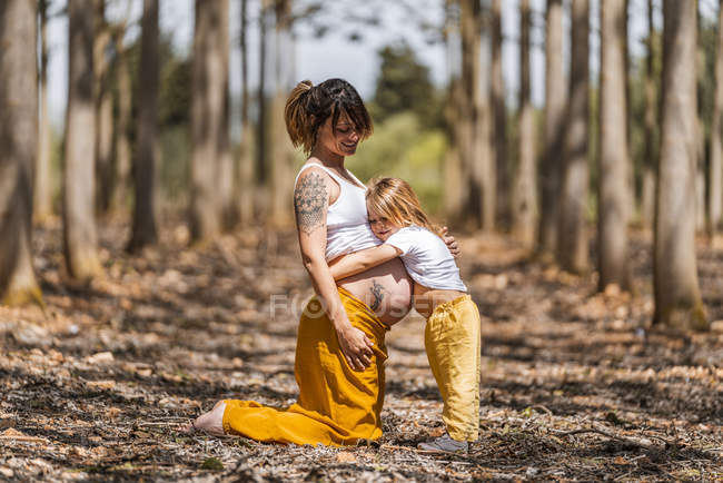 Madre embarazada y pequeña hija abrazándose en el parque de otoño - foto de stock