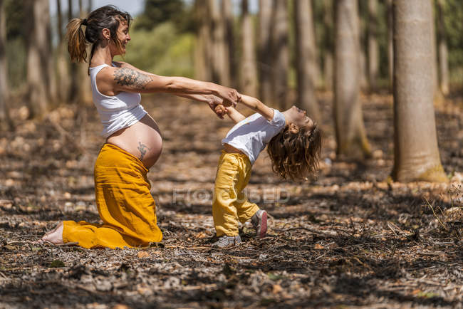 Madre embarazada e hija pequeña cogidas de la mano en el parque - foto de stock