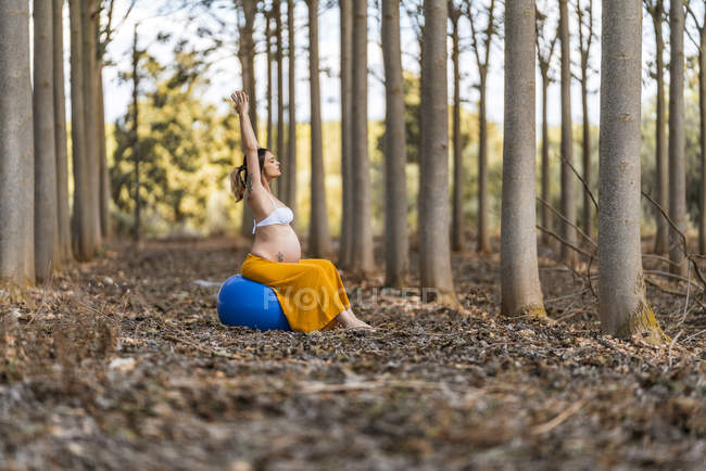 Adult pregnant lady sitting on big pilates ball in park during sunny daytime — Stock Photo