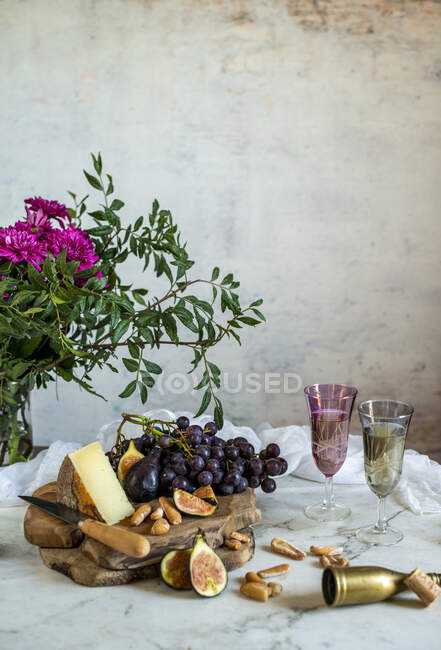 Uvas junto a trozo de queso en tablas de cortar cerca de flores rosadas — Stock Photo