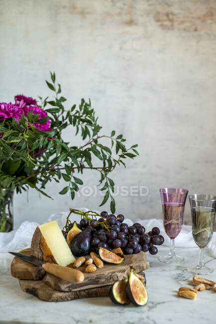 Виноград рядом с кусочком сыра на досках возле розовых цветов — стоковое фото