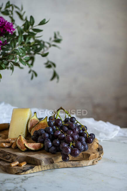 Uvas junto a trozo de queso en tablas de cortar cerca de flores rosadas - foto de stock