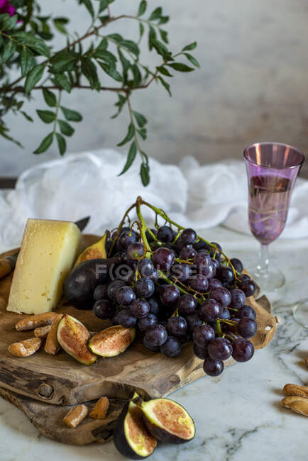 Uvas ao lado de pedaço de queijo em tábuas de corte perto de flores rosa — Fotografia de Stock