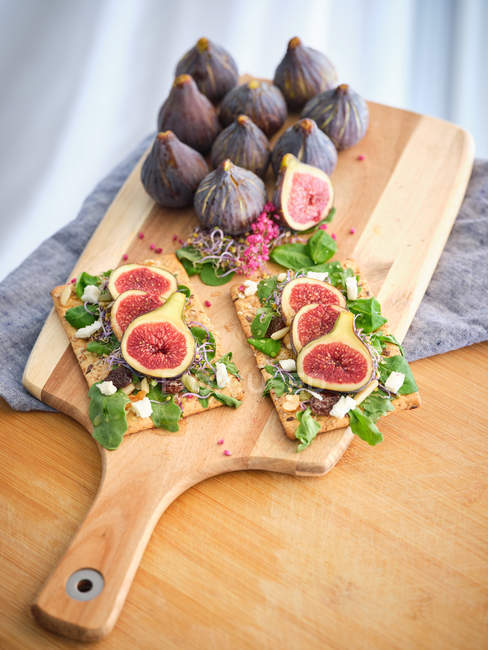 Hausgemachte offene Sandwiches mit Feigen- und Käsescheiben auf Roggenbrot mit Rucola auf Holzschneidebrett — Stockfoto