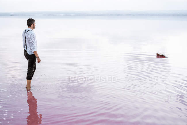 Side view serious man in white shirt and rolled up pants walking towards a guitar in gradient sea — Stock Photo