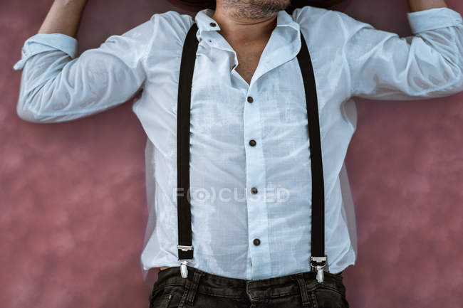 Vue du dessus de l'homme méconnaissable en chemise blanche et bretelles couchées en mer rose au banc de sable — Photo de stock