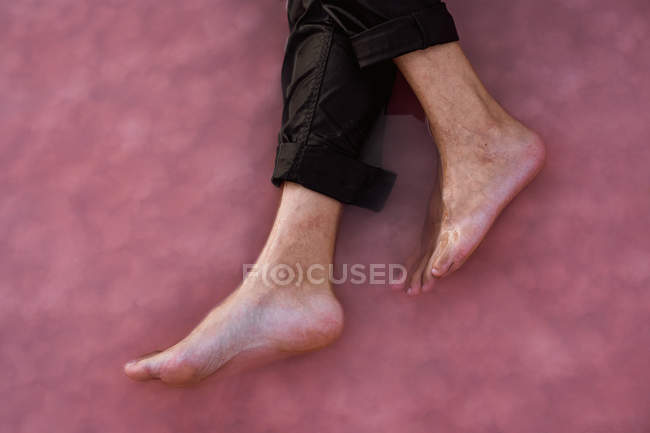 Обрізані чоловічі ноги в загорнутих штанях у морі на піщаному березі — стокове фото