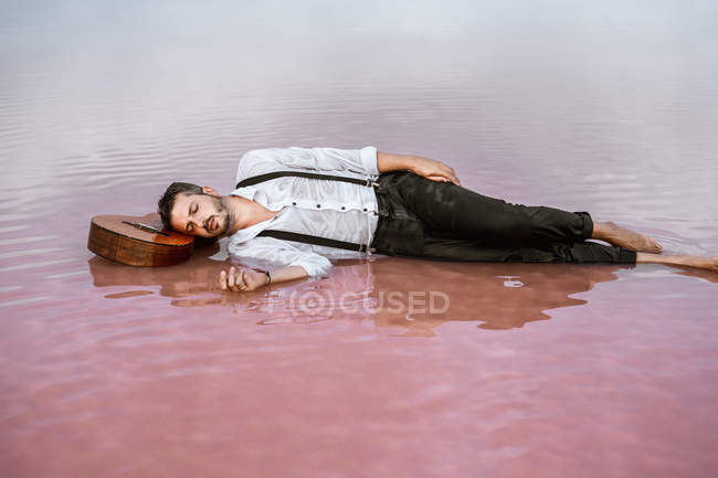 Sleepy hombre acostado con los ojos cerrados con la guitarra acústica en el mar en el banco de arena - foto de stock