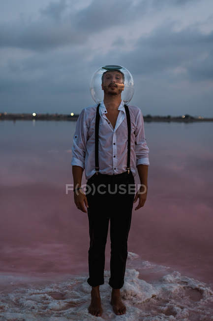 Hombre pensativo mirando en cámara en camisa mojada con acuario vacío en la cabeza de pie y contemplando por mar quieto en crepúsculo - foto de stock