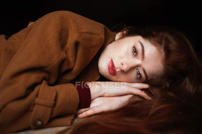 Mulher pensativa encantadora em casaco marrom deitado nas mãos e sonhando enquanto olha na câmera — Fotografia de Stock