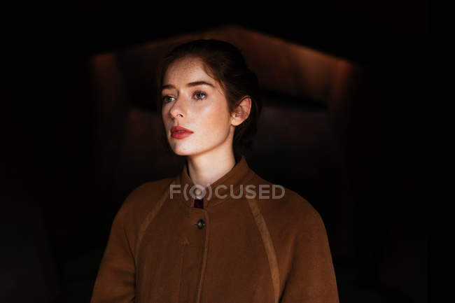 Pensive woman in coat looking away against black background — Stock Photo