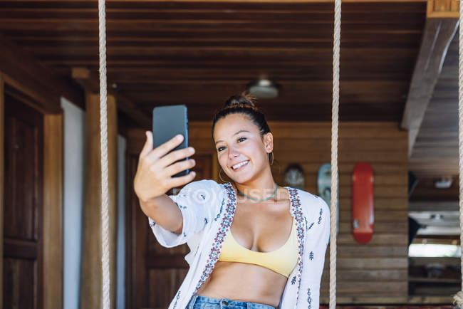 Mulher positiva tirando fotos no smartphone enquanto estava em quarto ensolarado com paredes de madeira na Costa Rica — Fotografia de Stock