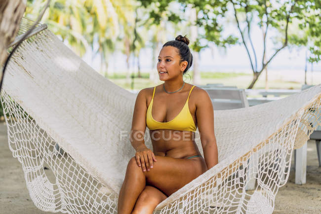 Delighted woman in swimsuit sitting in hammock and looking away at exotic seaside in Costa Rica — Stock Photo