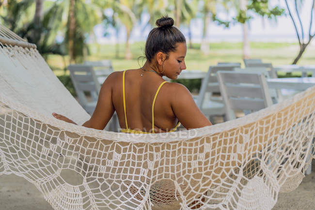 Vue arrière de la femme ravie en maillot de bain assis dans un hamac et regardant vers le bas au bord de la mer exotique au Costa Rica — Photo de stock