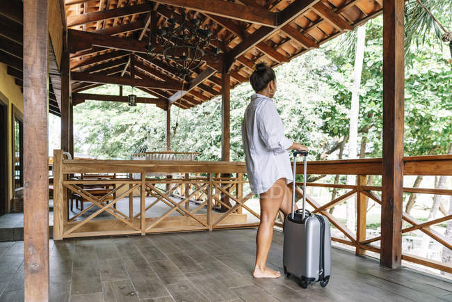 Vista lateral de la mujer que lleva equipaje mientras camina descalza a lo largo del patio rural de madera en el soleado resort en Costa Rica - foto de stock