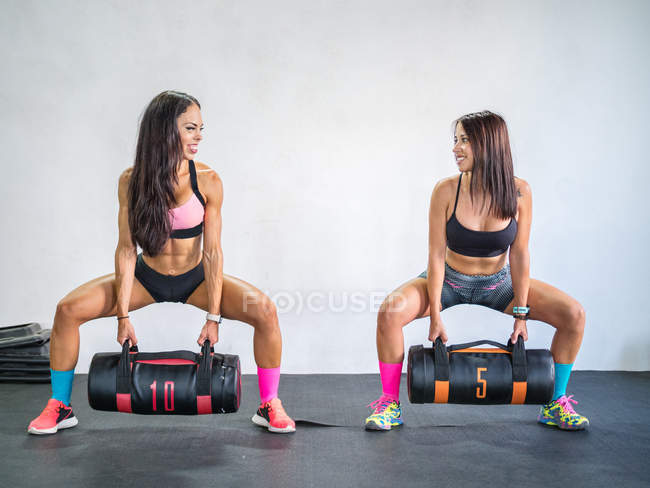 Happy sportswomen training with sand bags in modern gym — Stock Photo